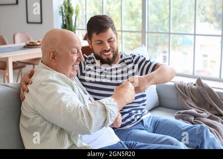 Glücklicher Mann und sein Vater stoßen sich mit den Fäusten, während er zu Hause auf dem Sofa sitzt Stockfoto