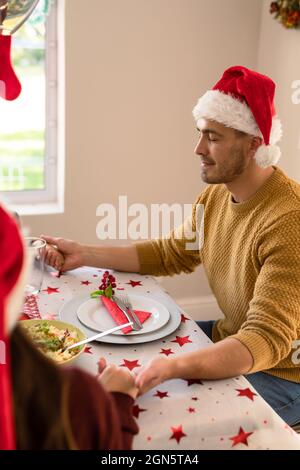 Kaukasischer Mann mit weihnachtsmütze, der am weihnachtstisch betet Stockfoto