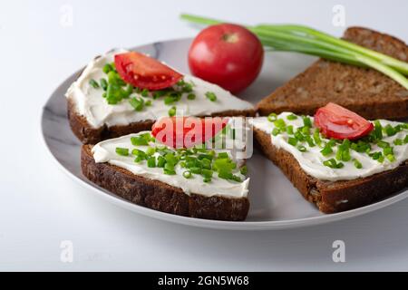 Brotscheiben mit Quark, Zwiebeln und Tomaten auf dem Teller Stockfoto