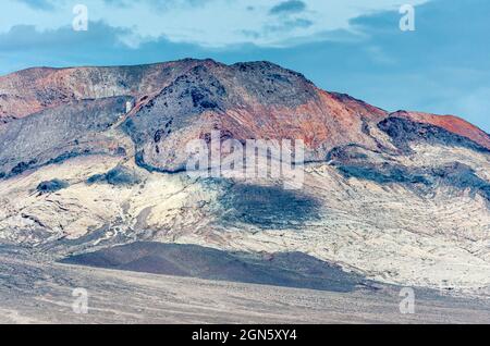 High Desert, Nevada, USA - 17. Mai 2011: Nahaufnahme von hohen mineralreichen farbigen Bergen und schwarzen Hügeln unter blauer Wolkenlandschaft. Stockfoto