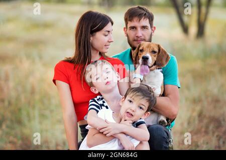 Gruppe von vier Personen, die Spaß beim Spielen mit Haustieren in ländlichen Gebieten haben. Vater, Mutter, zwei Söhne mit reinrassiger Beagle-Hündin. Authentizität Im Familienleben. Tiere und Freundschaft. Das Leben auf dem Land Stockfoto