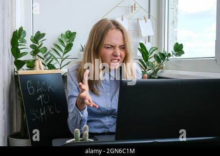 Müde, müde, junge kaukasische Arbeiterin am Schreibtisch. Überarbeit und Schlafentzug. Geschäftsfrau und Währungskrise. Freiberufler in Depressionen. Traurige Frau, die am Arbeitsplatz einen Laptop ansieht Stockfoto