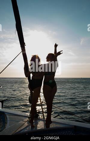 Zwei junge Frauen ruhen sich bei Sonnenuntergang auf einer Yacht im offenen Meer aus. Stockfoto