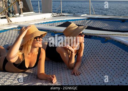 Zwei junge Frauen ruhen sich bei Sonnenuntergang auf einer Yacht im offenen Meer aus. Stockfoto