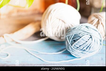 Kugeln aus weißem und beigem Garn auf hellblauem Holztisch. Fäden aus hochwertiger Wolle für Macrame und Kunsthandwerk. Stockfoto