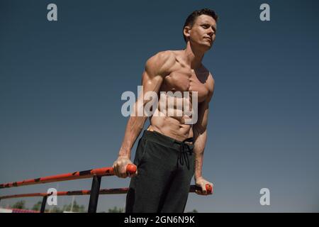 Sportler Mann macht Trizeps Dips auf parallelen Bars in Outdoor-Übungen. Kalisthenisch. Street Workout Stockfoto