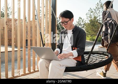 Horizontale mittellange Aufnahme einer modernen jungen asiatischen Frau, die Freizeitkleidung mit Brille trägt und Zeit im Freien verbringt Stockfoto