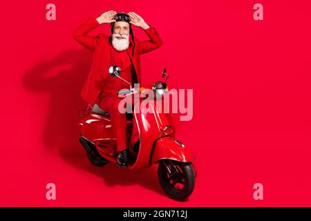 Foto von ziemlich gut aussehend reifen Motorradfahrer gekleidet weihnachten Kostüm Helm Arme Brille isoliert rote Farbe Hintergrund Stockfoto