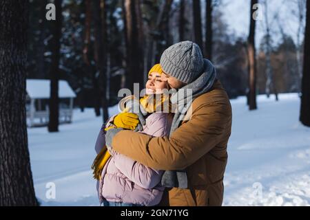 Mann in Strickmütze umarmt hübsche Freundin im Winter Park Stockfoto