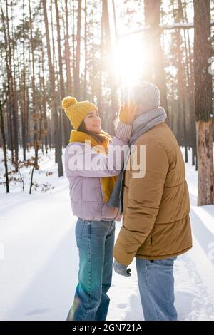 Glückliche Frau in gestricktem Hut berühren Gesicht des Freundes in verschneiten Park Stockfoto