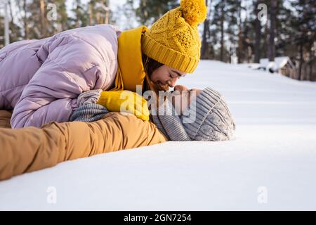 Seitenansicht eines jungen Paares in Hüten, die sich küssen, während sie auf Schnee liegen Stockfoto