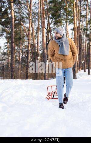 Positiver bärtiger Mann, der im Winterpark Schlitten zieht Stockfoto
