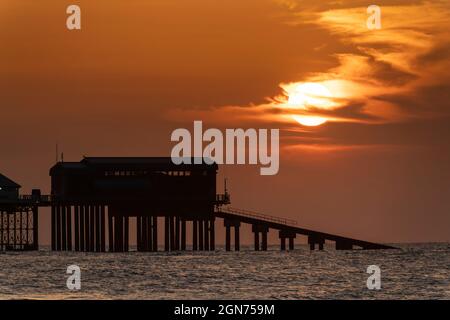 Blick auf den Sonnenuntergang über dem Cromer Pier, der das Ende des Pier-Theaters und die RNLI-Rettungsbootstation zeigt, Cromer, Norfolk, Großbritannien Stockfoto