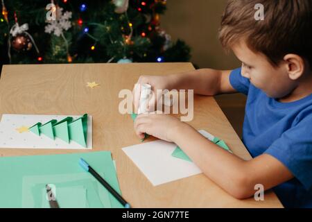 Schritt 5: Weihnachtskarte erstellen. Kleben Sie die vorbereiteten Teile des Weihnachtsbaums auf das Kartenblatt. Zwei Karten für Weihnachten von den Händen eines Erwachsenen und eines Kindes gemacht. Stockfoto