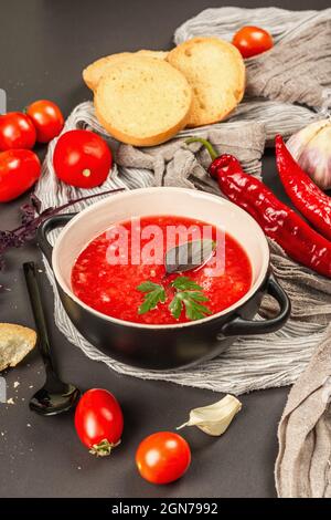 Veganes Essen, würzige Gazpachosuppe mit Tomaten, reifes Gemüse und frische Basilikumkräuter. Schwarzer Stein Beton Hintergrund, Nahaufnahme Stockfoto