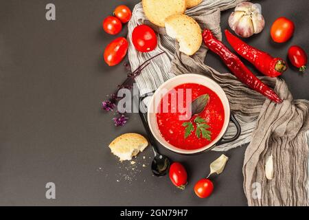 Veganes Essen, würzige Gazpachosuppe mit Tomaten, reifes Gemüse und frische Basilikumkräuter. Schwarzer Stein Beton Hintergrund, Draufsicht Stockfoto