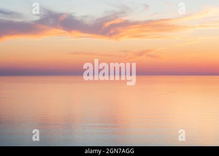 Whiskey-Wolken bei Sonnenuntergang über einem ruhigen Meer Stockfoto