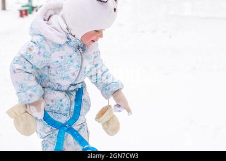 Mädchen mit Schneefall auf Spielplatz zwischen Häusern im Winter. Aktive Schneeballspiele auf der Straße Stockfoto