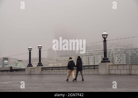 An einem trüben Tag laufen die Menschen an einer kaum sichtbaren Skyline der City of London vorbei. Dichter Nebel verschlang viel von der Hauptstadt, als die Temperaturen fielen. London, Großbritannien 3. März 2021. Stockfoto