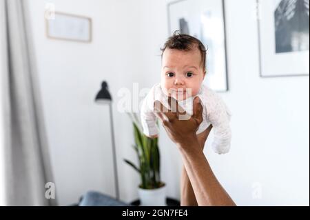 Nettes Baby Mädchen in den Händen ihres Vaters. Nahaufnahme des Porträts einer kleinen Tochter, die die Kamera anschaut, während die Familie zu Hause spielt Stockfoto