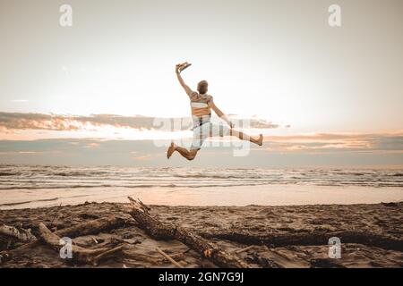 Fröhlicher Junge, der Sommerferien am Strand bei Sonnenuntergang genießt - junger Mann, der beim Sonnenaufgang am Strand springt - Urlaubskonzept6 Stockfoto