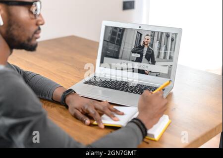 Arbeitsloser Mann mit Laptop, durchsuchen Sie die Unternehmenswebsite. Fokussierter afroamerikanischer Mann sucht einen Job und schreibt einen Lebenslauf. Verzweifelter Kerl sucht verschiedene Möglichkeiten für seine Spezialität Stockfoto