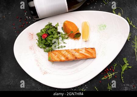 Gegrilltes Lachssteak auf dunklem Hintergrund mit einer Flasche Wein im Hintergrund Stockfoto