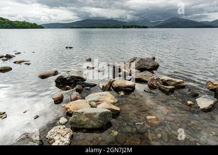 Entlang des West Highland Way in Schottland. Ein Blick vom Ufer des Loch Lomond, wo einige Steine die Oberfläche des klaren Wassers des Sees berühren Stockfoto