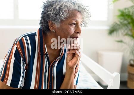 Porträt einer nachdenklichen afroamerikanischen älteren Frau, die auf dem Bett sitzt und in die Ferne blickt Stockfoto