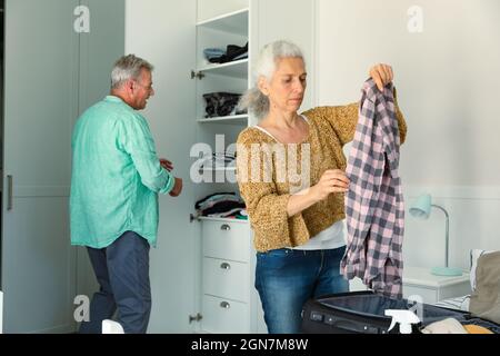 Fokussiertes kaukasisches Senior-Paar, das Koffer im Schlafzimmer zusammenpackt Stockfoto