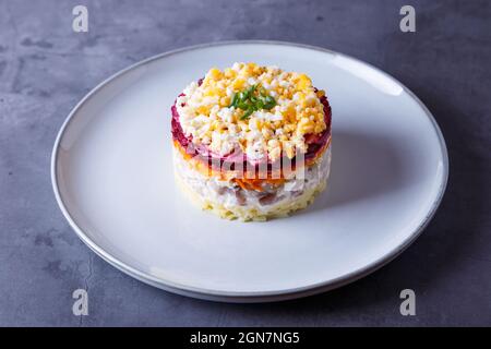 Heringsalat unter einem Pelzmantel. Traditioneller russischer, vielschichtiger Salat aus Hering, Rüben, Kartoffeln, Karotten und Eiern. Nahaufnahme, grauer Hintergrund. Stockfoto