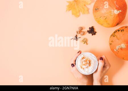 Herbstgetränk Kürbisgewürz Latte in weiblichen Händen neben Zutaten auf orangefarbenem Hintergrund mit Kopierfläche Stockfoto