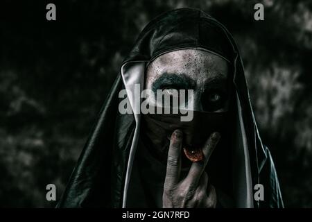 Eine furchterregende böse Nonne, in einer typischen schwarz-weißen Angewohnheit, streckt ihre durchbohrte Zunge durch ein Loch in ihrer schwarzen Gesichtsmaske aus Stockfoto