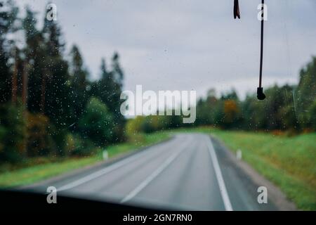 Regenwassertropfen auf dem Fenster. Blick auf die Straße und den Herbstwald durch das Busfenster. Roadtrip. Schöne Herbstnatur Stockfoto