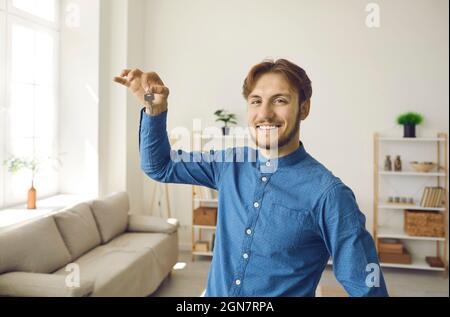 Porträt eines glücklichen jungen Mannes, der lächelt und uns die Schlüssel zu seinem neuen Haus oder seiner Wohnung zeigt Stockfoto