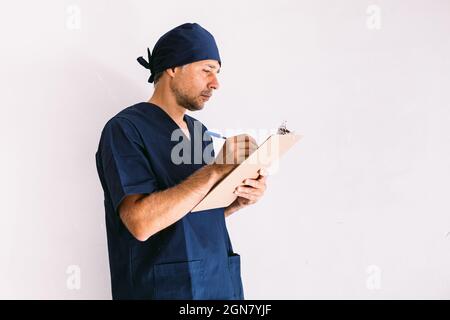 Krankenschwester, Arzt oder Tierarzt in blauer Uniform an einem Fenster in einem Krankenhaus, der einen Bericht verfasst. Medizin-, Krankenhaus- und Gesundheitskonzept. Stockfoto
