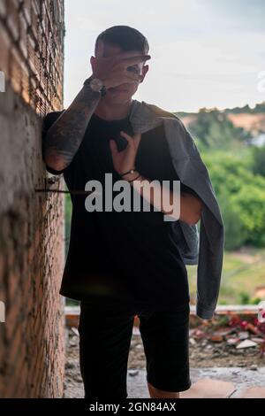 Porträt eines jungen hübschen kaukasischen Mannes in lässiger schwarzer Kleidung, der durch die Finger schaut. Blick auf die Kamera. Jacke mit HalteDenim Stockfoto