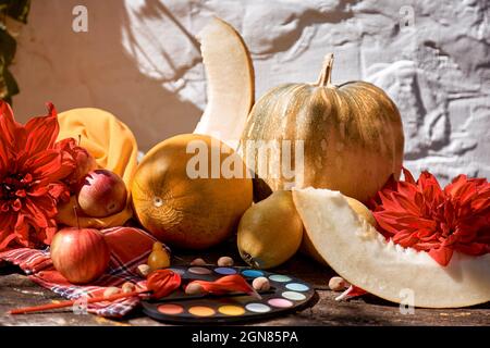 Herbst modernes Stillleben mit trendigen Schatten: Gelbes Gemüse, Obst und helle Farben mit Pinsel, Kürbis, Birnen, Apfel und Melone. Thanksgiving Day Konzept. Herbst rot georgine Dekoration. Stockfoto