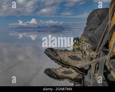 UYUNI, BOLIVIEN - 06. Feb 2018: Ein Mann, der große Wanderschuhe trägt, hängt seine Beine vom Dach eines 4x4, der auf Boliviens Salar de Uyuni leer fährt, Ref Stockfoto