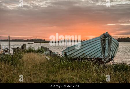 Holzboot mit Seil im Bug, bei Sonnenuntergang auf einer Strandwiese vertäut, Bisserup, Dänemark, 8. August 2021 Stockfoto