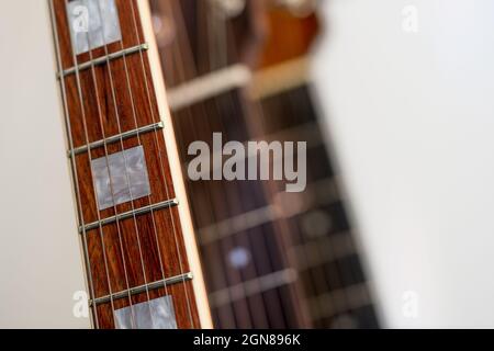 Nahaufnahme eines Palisander Perlmutt-Griffbretts mit sechs Saiten auf einer E-Gitarre mit Gitarren, die im Hintergrund unscharf sind Stockfoto