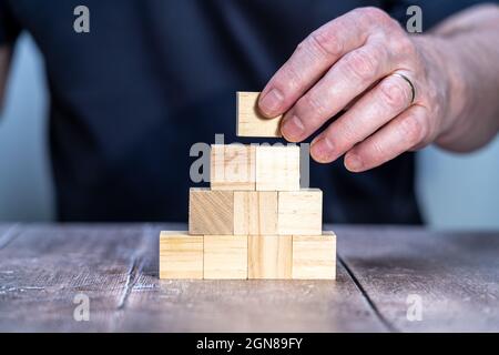 Mann, der einen Holzblock hält, um eine leere Schablone mit einer Pyramide aus zehn Holzblöcken zu erstellen Stockfoto