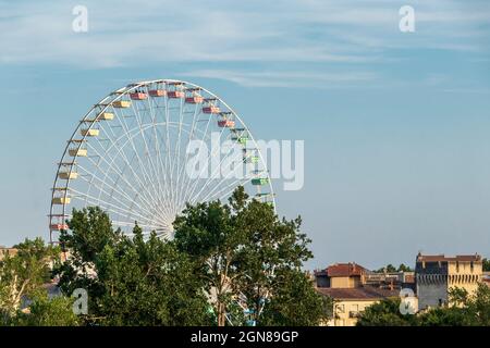 Riesenrad oder Panoramarad in der Stadt Avignon mit historischem Denkmal im Hintergrund, mittelalterliche Stadtmauern mit Türmen aus Kalkstein Stockfoto