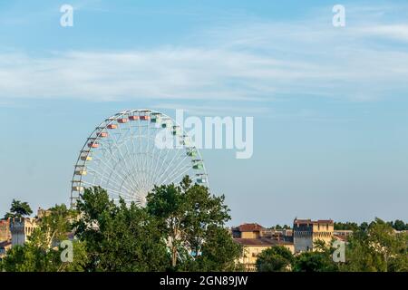 Riesenrad oder Panoramarad in der Stadt Avignon mit historischem Denkmal im Hintergrund, mittelalterliche Stadtmauern mit Türmen aus Kalkstein Stockfoto