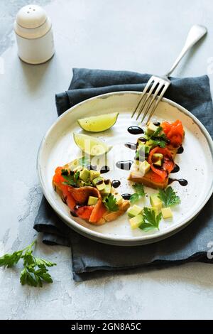 Avocado- und Lachsbrote mit Balsamico-Sauce und Koriander auf altem Olivenbrett. Draufsicht Stockfoto