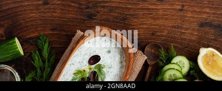 Traditionelle griechische Sauce Tzatziki in olivfarbener Holzschüssel auf altem rustikalen Hintergrund. Draufsicht. Stockfoto