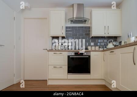 Moderne Einbauküche im cremefarbenem Shaker-Stil mit eingebauten Geräten mit grauen Splashback-Fliesen und Dunstabzugshaube aus Edelstahl mit Extrakt und w Stockfoto