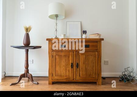 Esszimmer Interieur aus Eiche Seitenwand mit imitierten silbernen Bilderrahmen, Bücher, Lampe und porzellan Topf mit antiken Sockel Tisch und Vase mit Weizen r Stockfoto