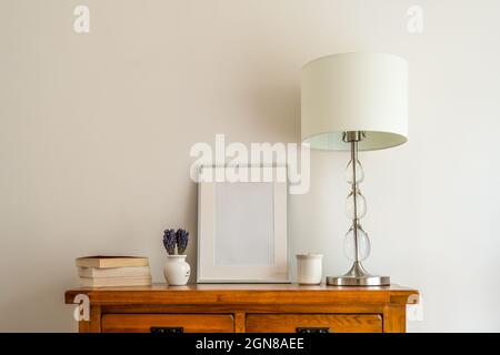 Nahaufnahme der inneren Eiche-Seitenwand mit imitiertem silbernen Bilderrahmen, Büchern, Lampe mit Schirm und porzellan-Topf und Lavendel-Blumenarrangement in Stockfoto