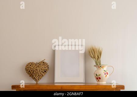 Nahaufnahme der inneren Eiche-Seitenwand mit imitiertem silbernen Bilderrahmen, Rattan-Herz und porzellankrug mit Weizenrye-Blumenarrangement Stockfoto